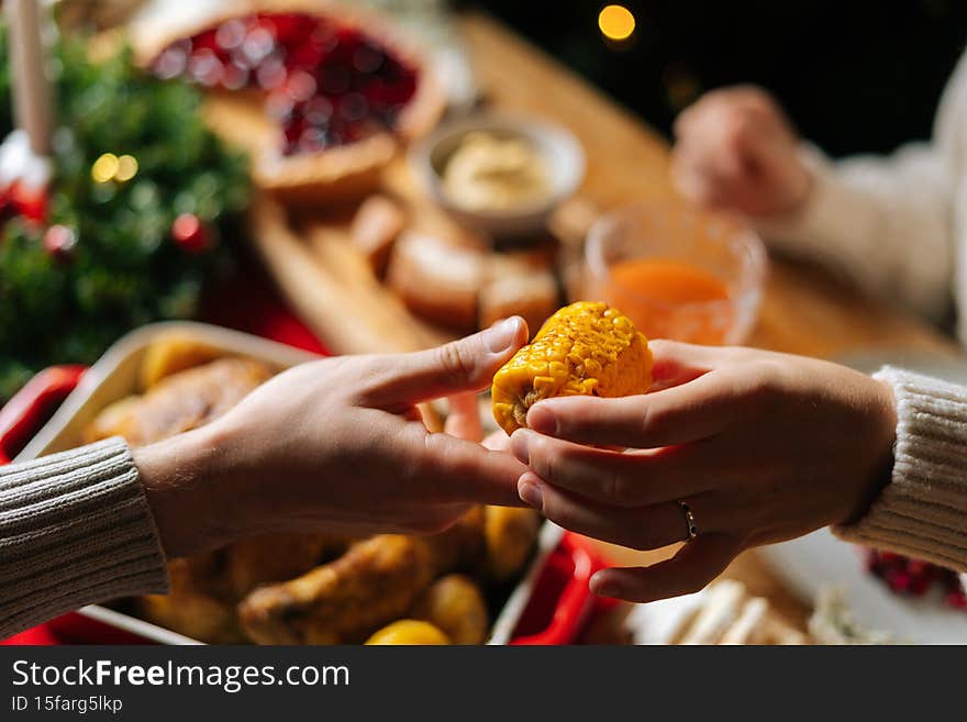 Close-up top view of unrecognizable young woman and man passing delicious boiled corn sitting at festive Christmas table