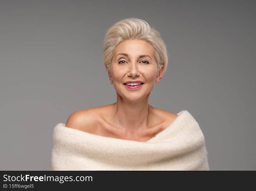 Beautiful blonde caucasian middle aged woman with short hairstyle. Attractive lady with delicate makeup and smile wearing warm fashionable sweater, posing in studio. A lot of copy space