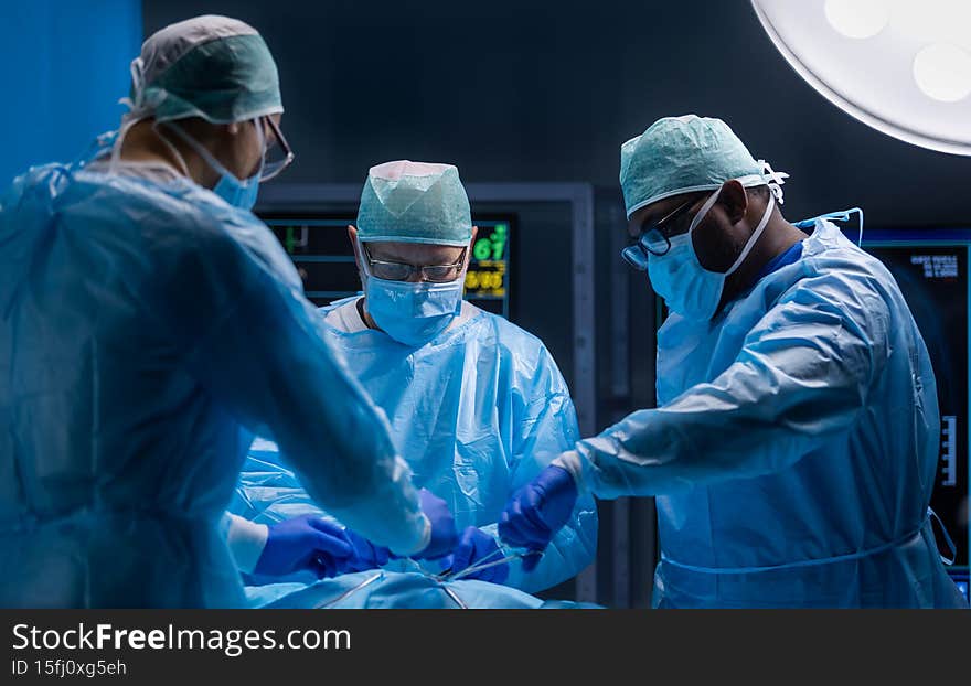 Multiracial team of professional medical surgeons performs the surgical operation in a modern hospital. Doctors are