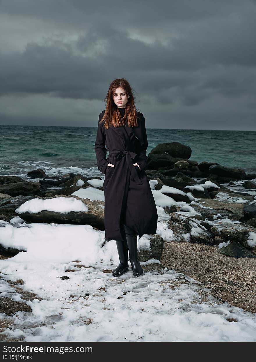 woman in a black coat outdoors landscape ocean dark clouds gothic
