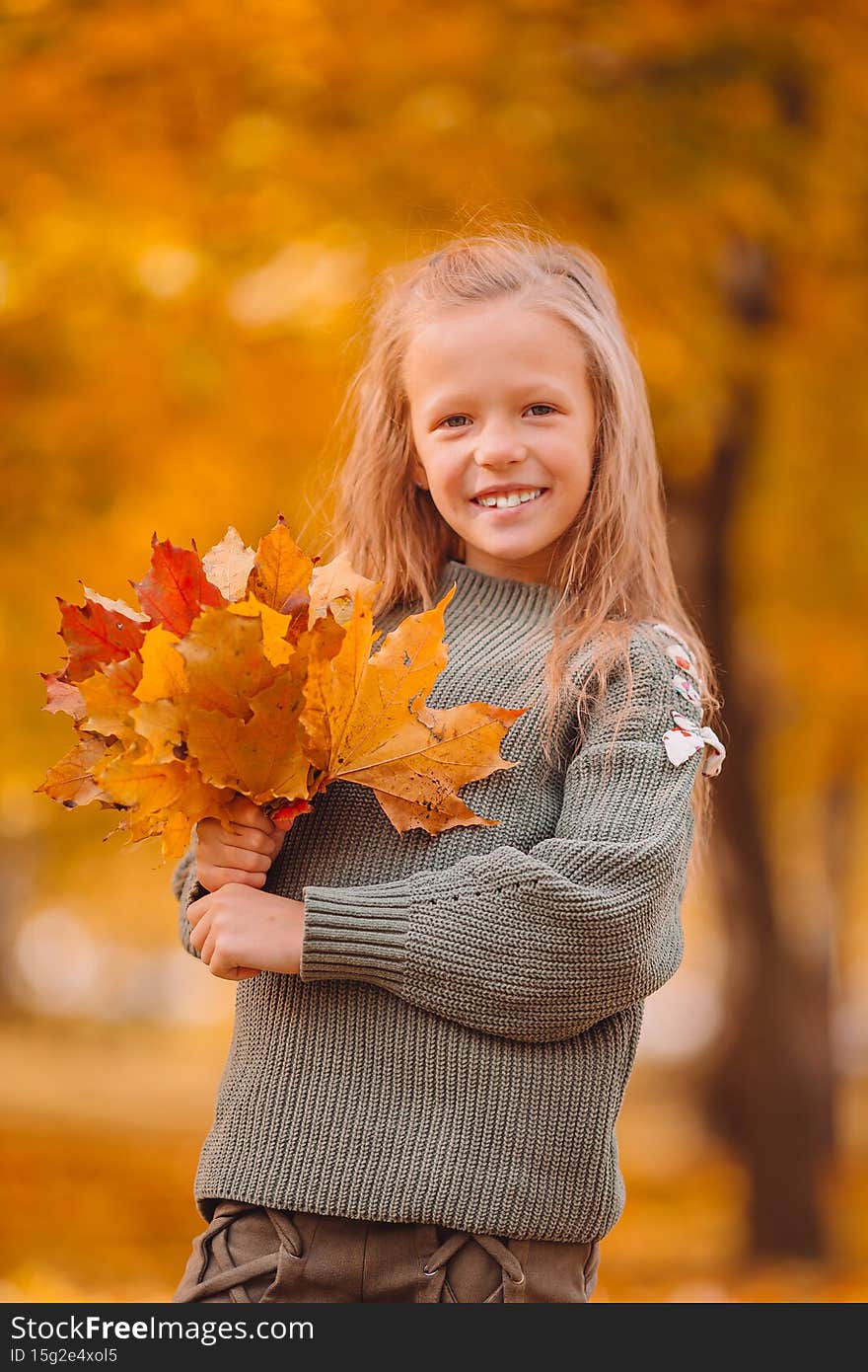 Portrait of adorable little girl with yellow leaves bouquet in fall
