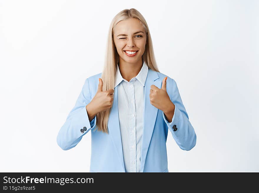 Ambitious businesswoman showing thumbs up and winking, recommending or praising smth good, give positive feedback