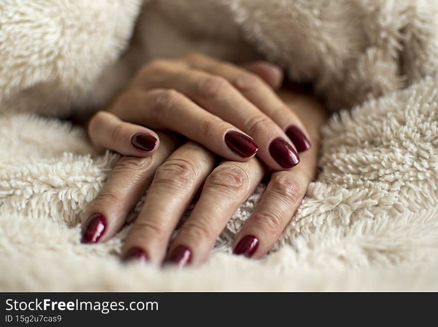 Wrinkled hand skin closeup. Dark red royal nail gel polish, female manicure, beauty treatment in a salon. Selective focus on the details, blurred background.