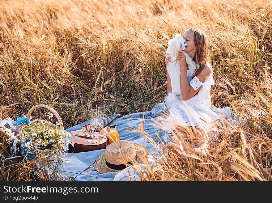 Little girl with puppy in wheat field. Beautiful girl in white dress in a straw hat with a bouquet of chamomile in hands. Little girl with puppy in wheat field. Beautiful girl in white dress in a straw hat with a bouquet of chamomile in hands