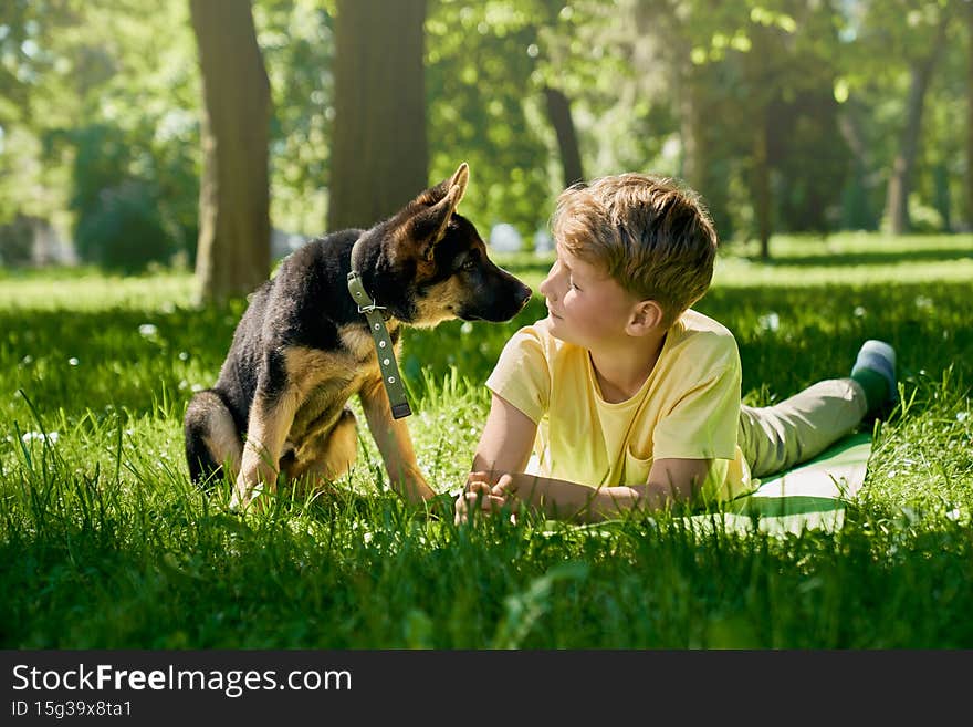 Teenager with puppy lying on grass at summer park