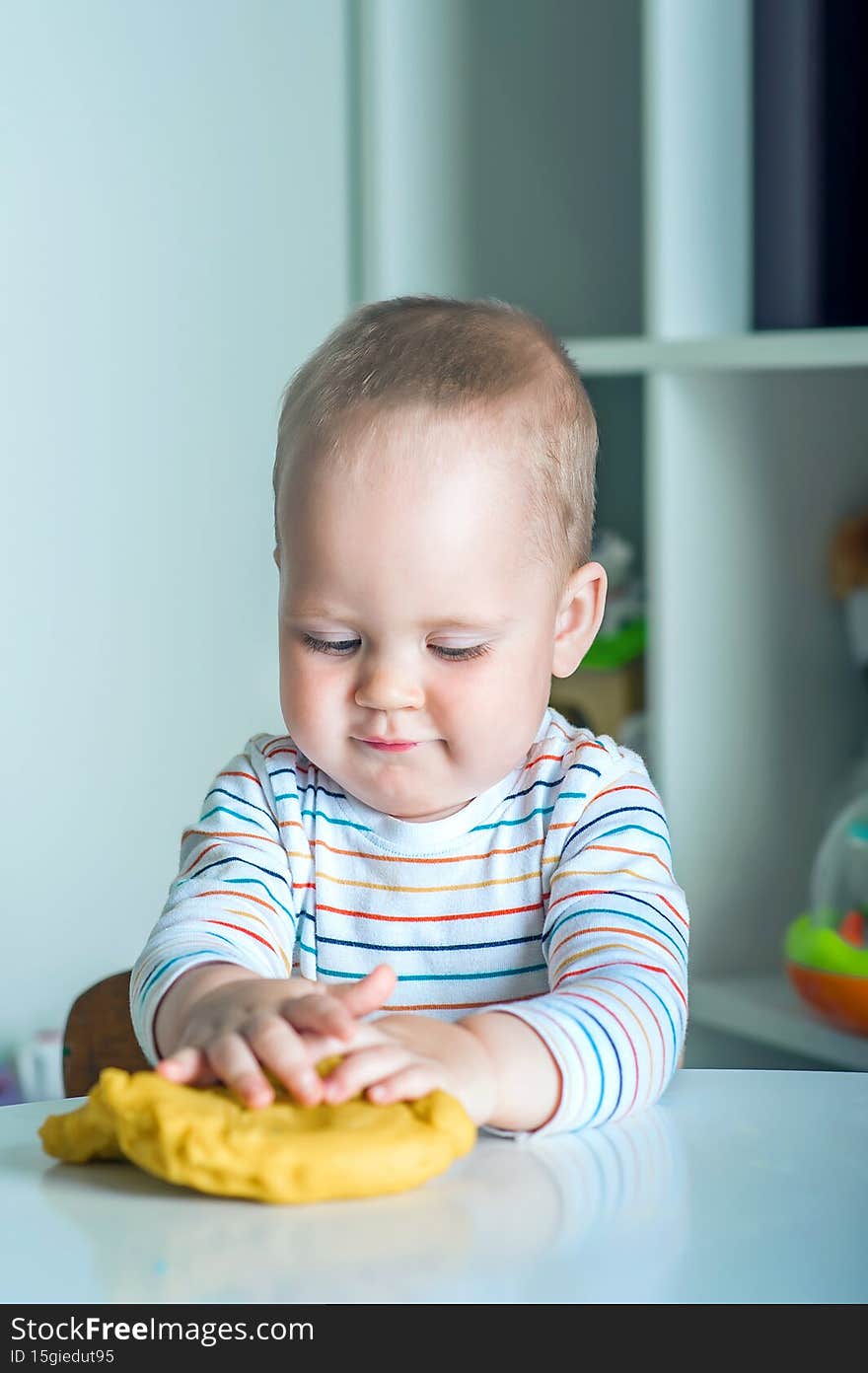 Toddler boy playing yellow plasticine Play-Doh in playroom close-up and copy space.