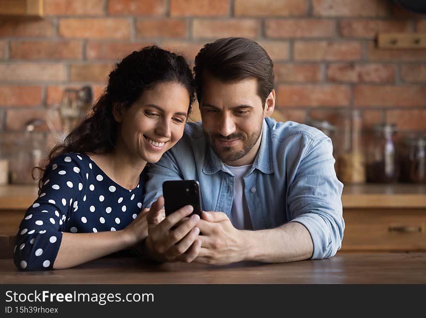 Loving young husband and wife embrace watch video on cellphone