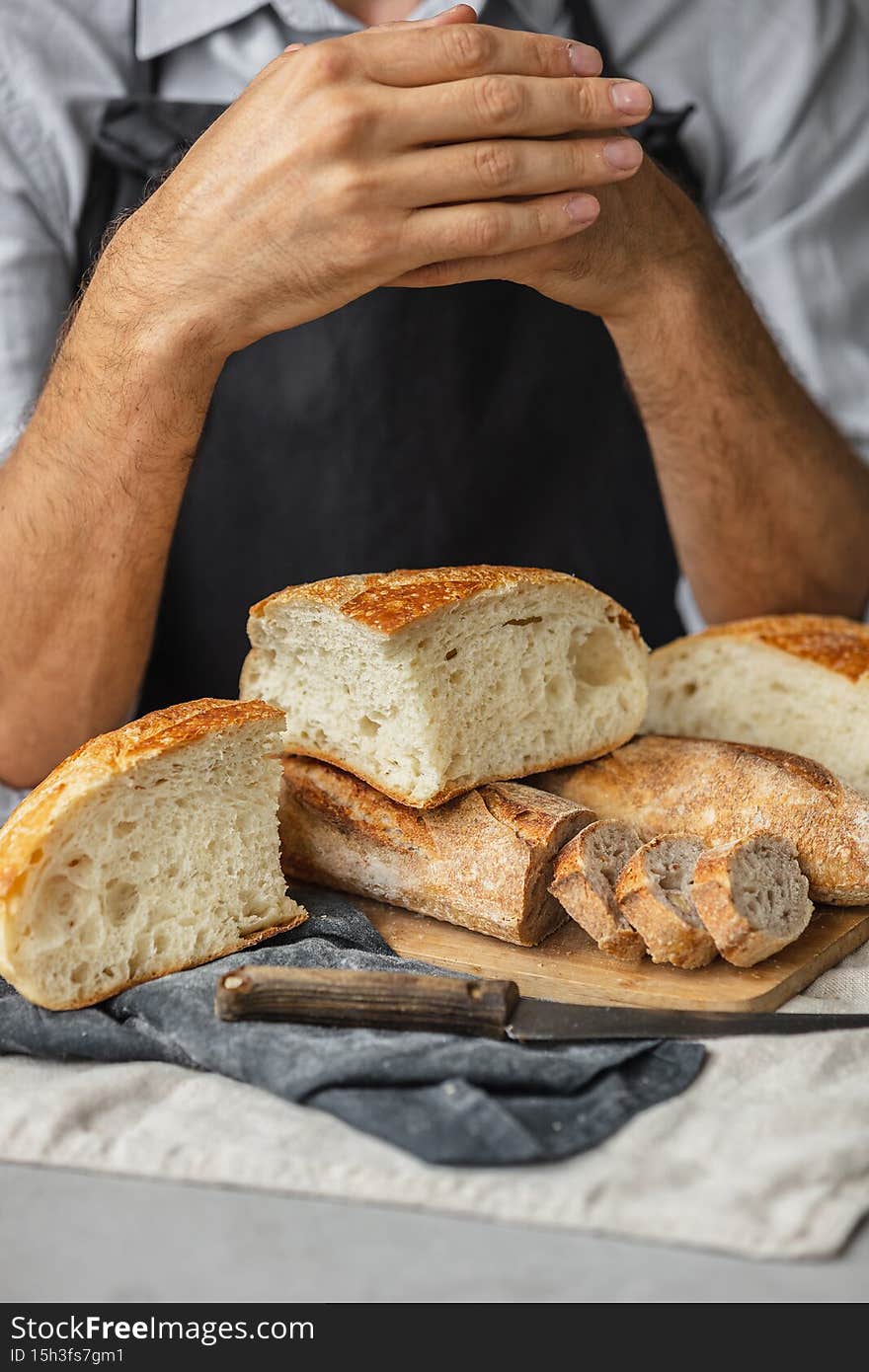an adult European male baker holds a round fresh bread in his hands. a man in a bakery holds a yeast-free bread on sourdough and a baguette. cool and healthy bread for the whole family. vegan food for lunch or dinner. a white man cuts bread with a knife on a wooden cutting board. photo of food, bakery or restaurant, ordering and delivery of food