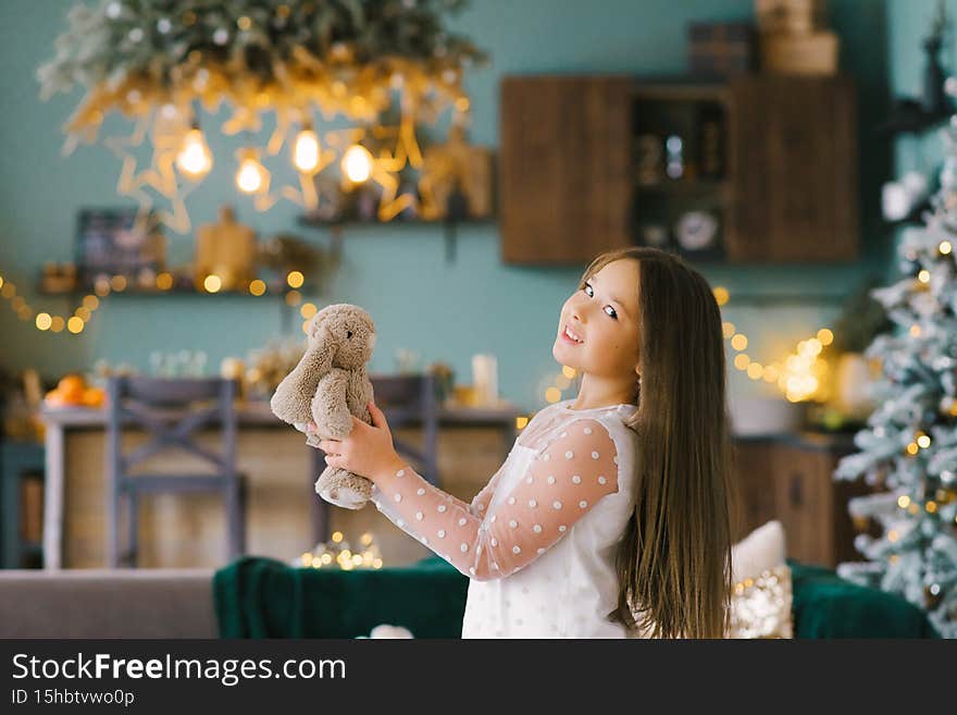 The concept of a happy New year. A girl stands near the Christmas tree and holds a stuffed Bunny in her hands. A little girl is happy with a Christmas gift.