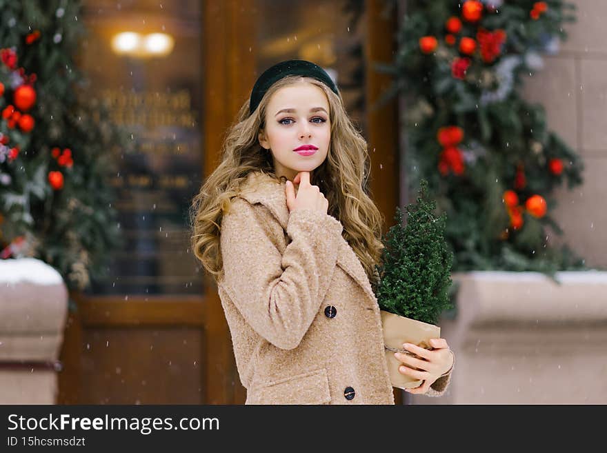 A stylish young woman walking around the city in winter, holding a potted Christmas tree in her hands. Christmas holidays