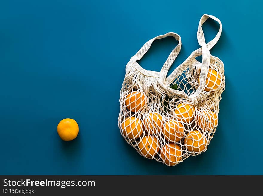 Mandarins or tangerines fruits in cotton eco-friendly mesh bag on blue background. Concept of zero waste, plastic-free shopping or eco food. Top view.
