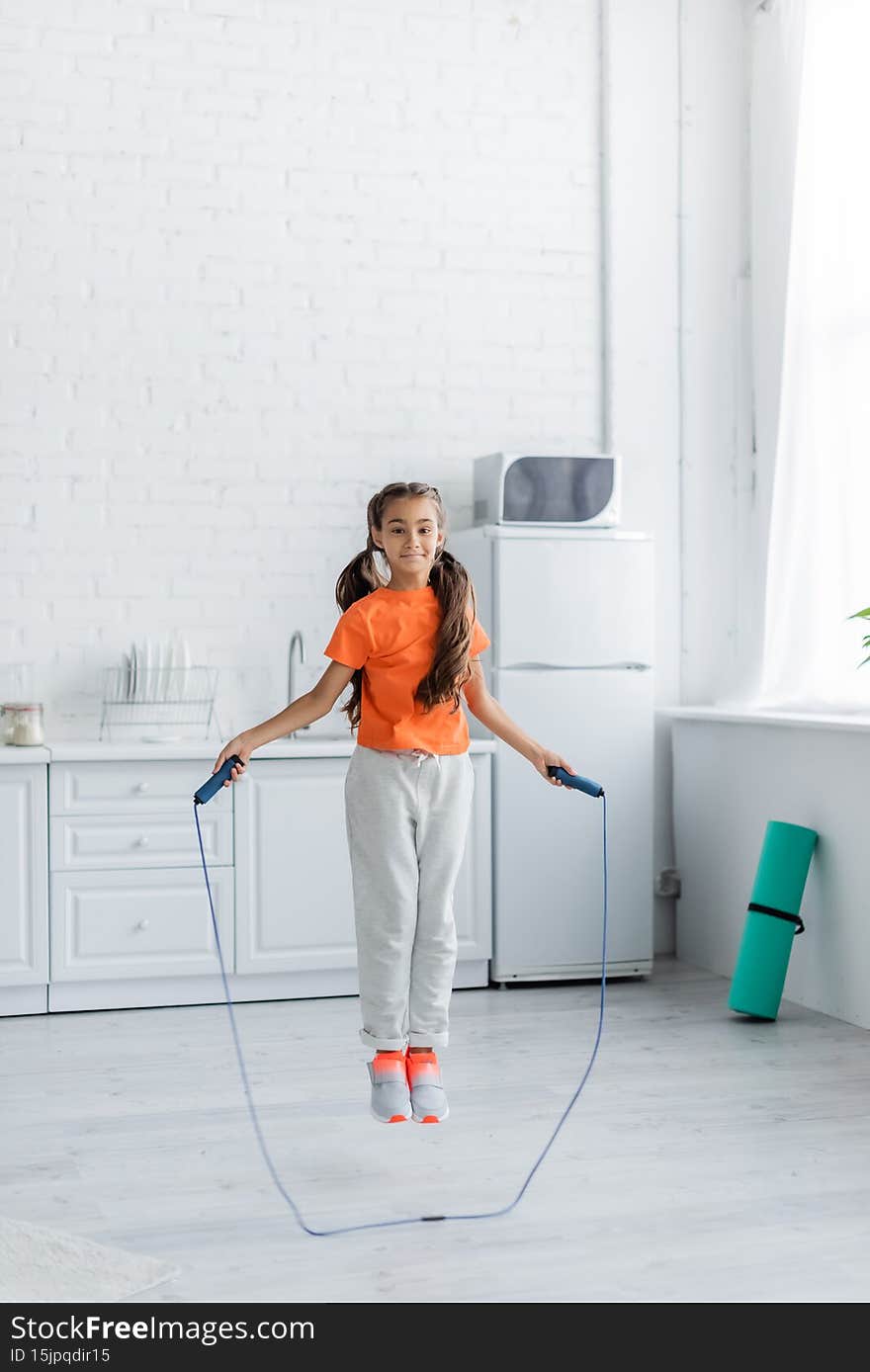 Smiling girl jumping with rope in kitchen at home,stock image