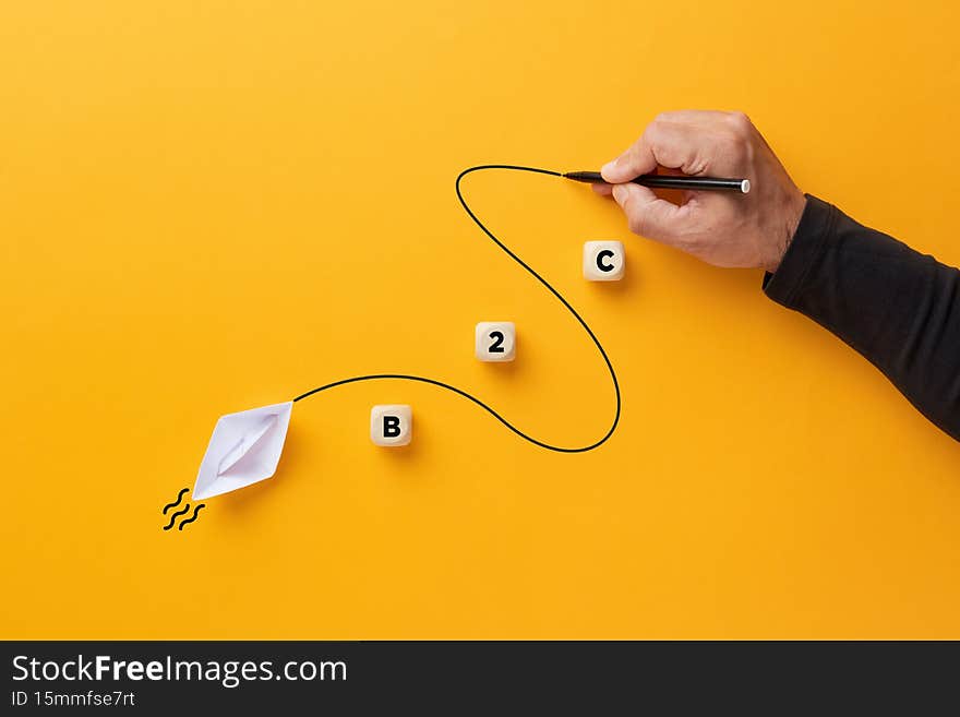 Male hand draws a curved line that guides a paper boat with the acronym B2C. Business to consumer or customer supply or transaction concept. Male hand draws a curved line that guides a paper boat with the acronym B2C. Business to consumer or customer supply or transaction concept