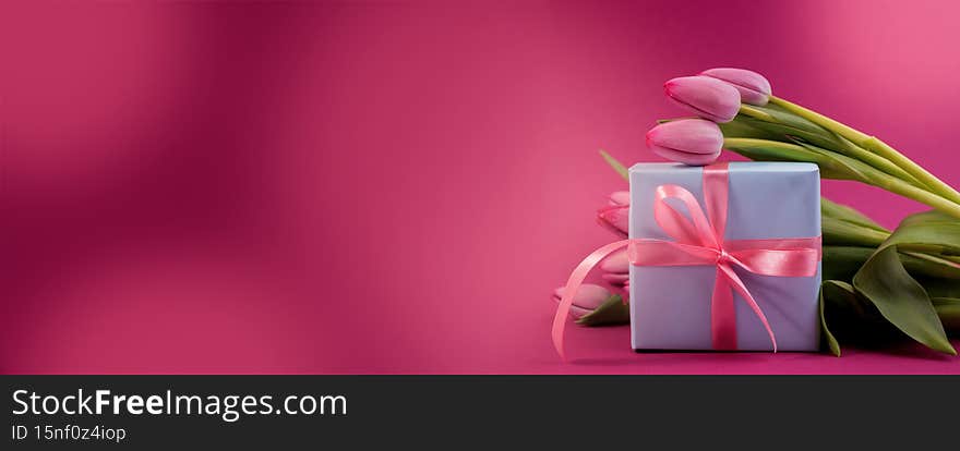 Romantic gift box tied with big pink bow and spring tulips on pink color background. Mother s day or Easter holiday