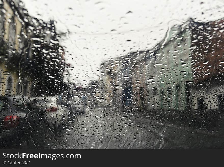 Wet glass, car inside view of street with buildings and houses
