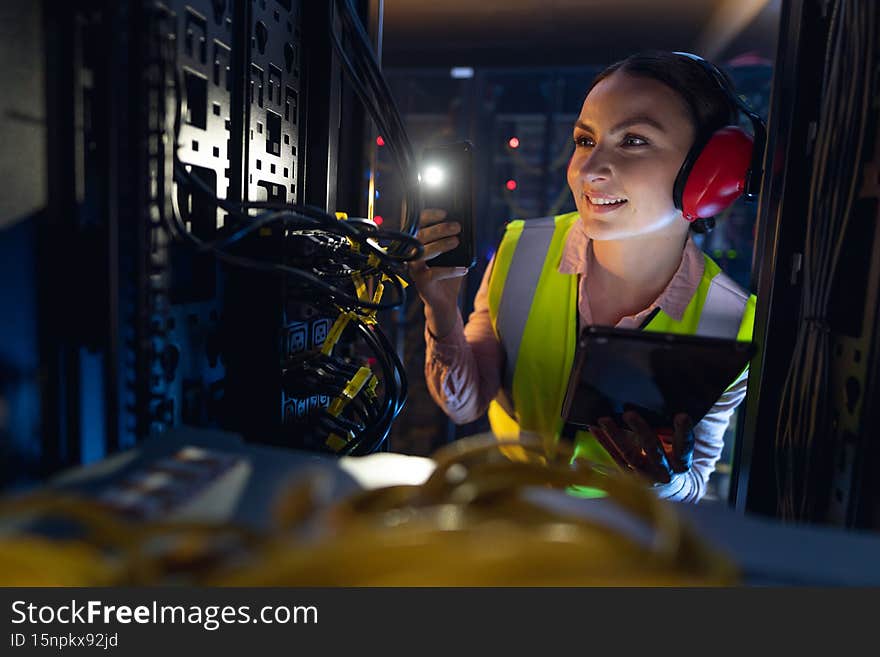 Caucasian female engineer using smartphone flash while inspecting the server in computer server room