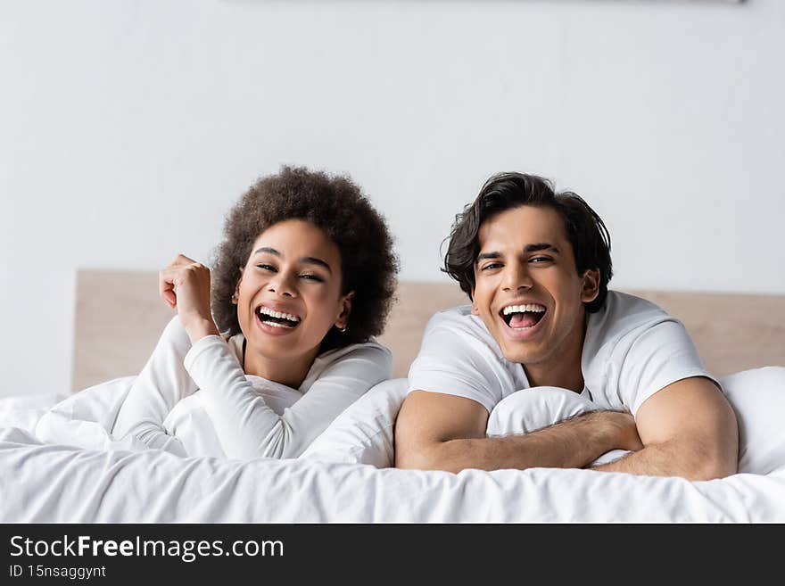 happy multiethnic couple laughing while lying in bed,stock image