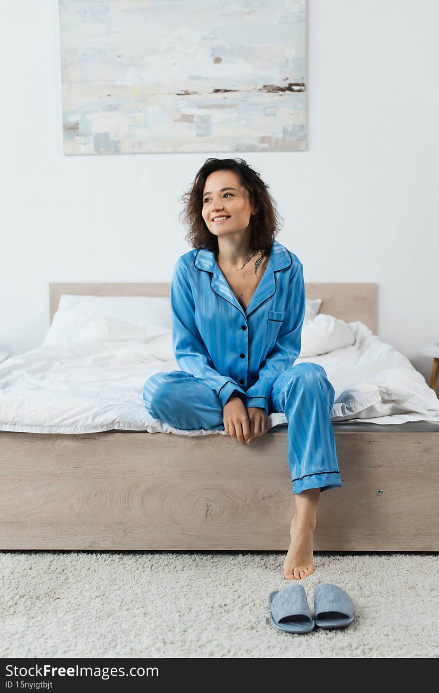 happy tattooed woman in pajamas sitting on bed,stock image