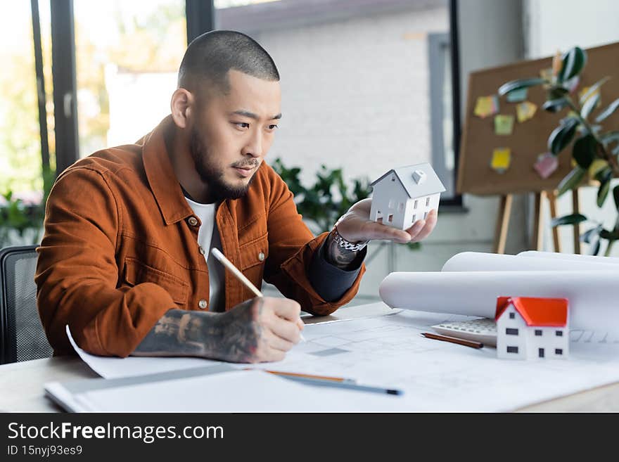 asian architect holding house model while drawing blueprint in office,stock image