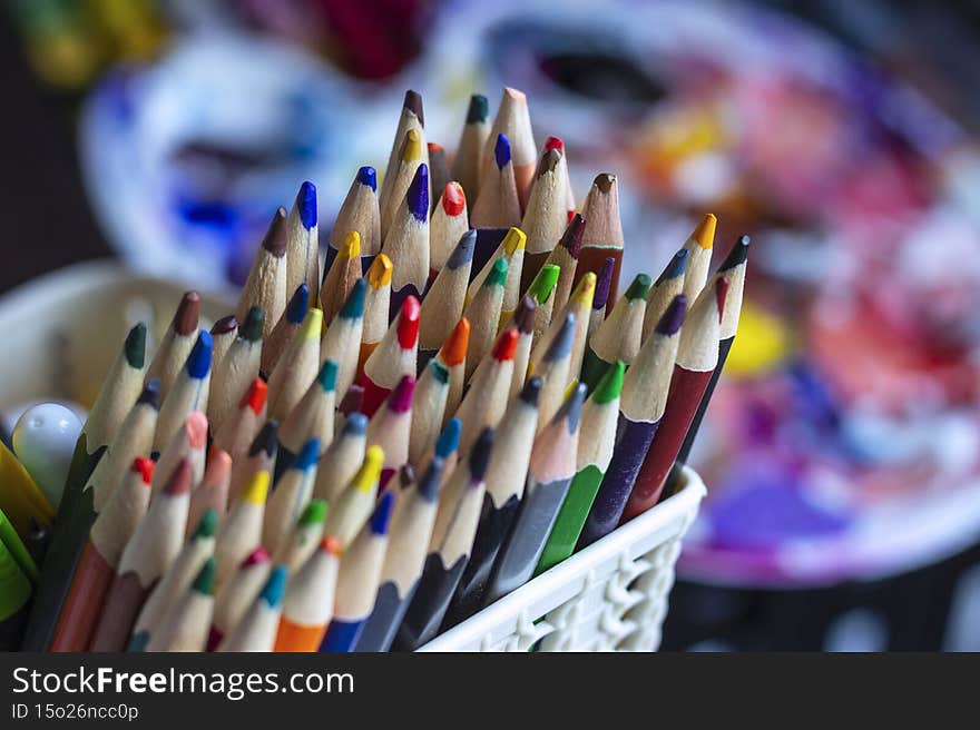 A set of colored pencils in a stand, against the background of art supplies.