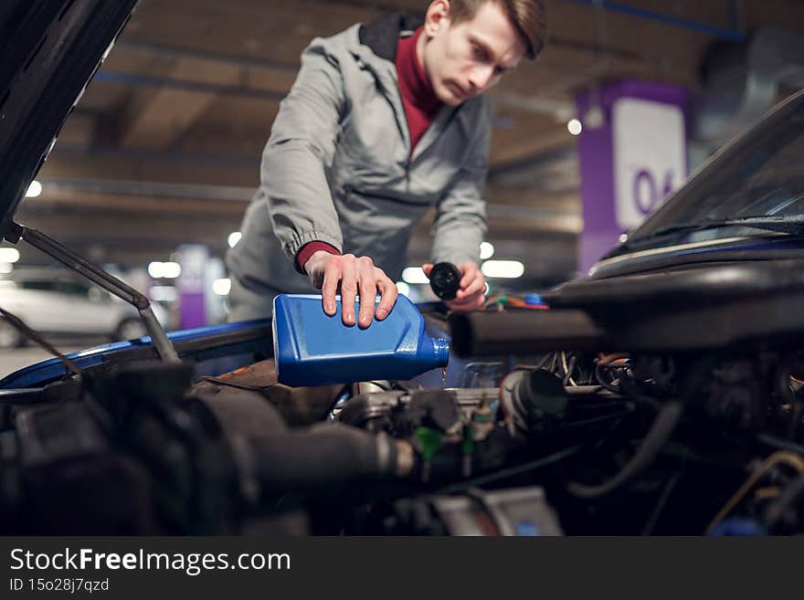 Man pouring oil in blue bottle in car with open hood, bokeh background