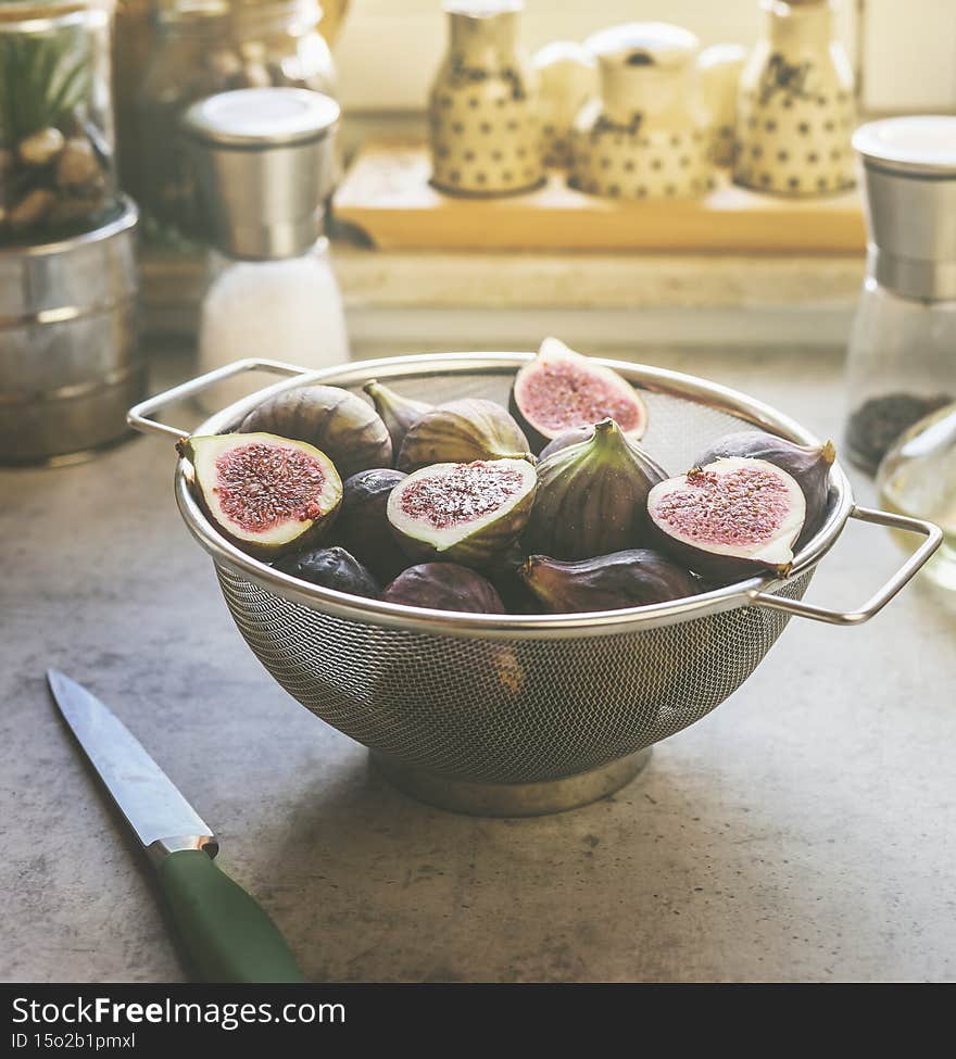 Fig halves in sieve on grey kitchen table with knife and kitchen utensils in background. Preparing healthy Mediterranean fruit at