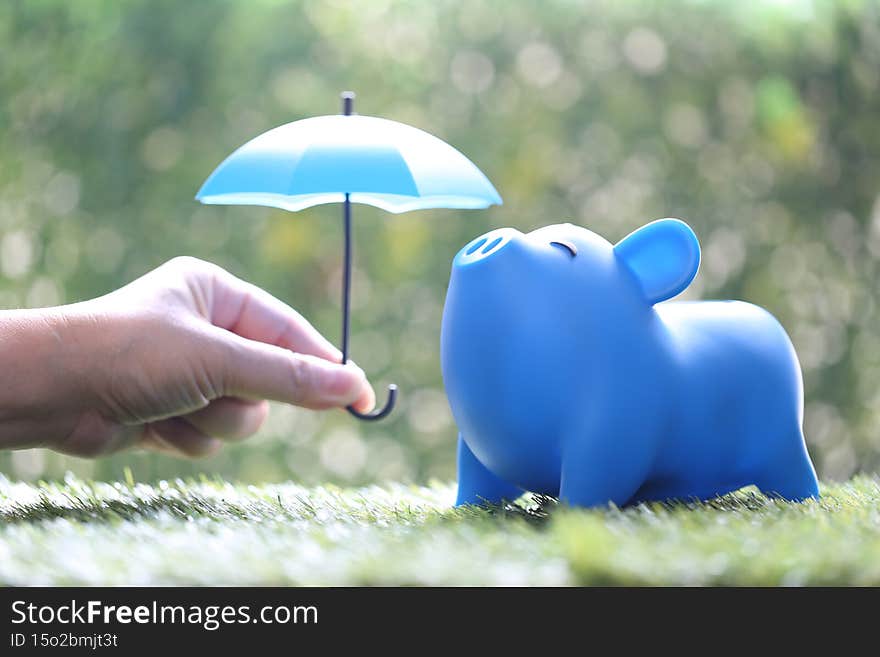 Protection,Piggy bank with hand holding the umbrella on natural green background, Finance insurance and Safe investment concept
