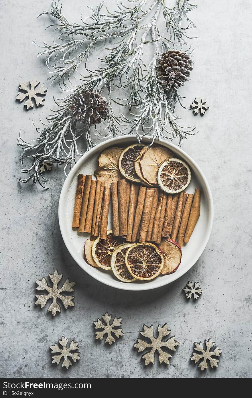 Winter spices on white plate with fir green, pine cones and wooden snowflakes on pale grey kitchen table. Mulled wine preparation