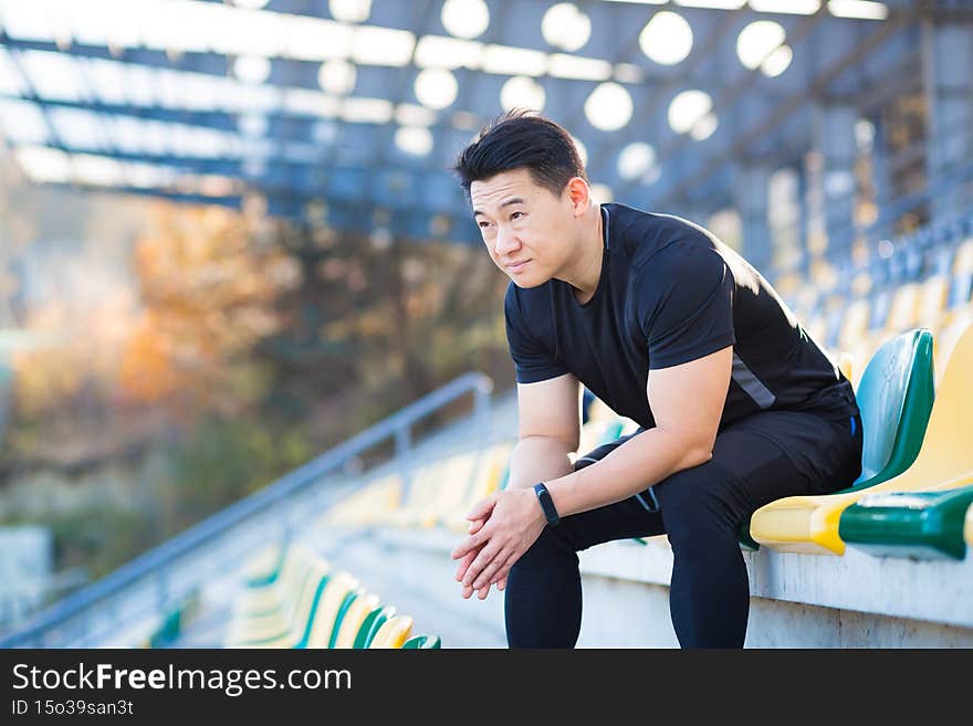 Frustrated Asian male athlete depressed, dissatisfied with the result of his training, in despair after running, resting sitting.