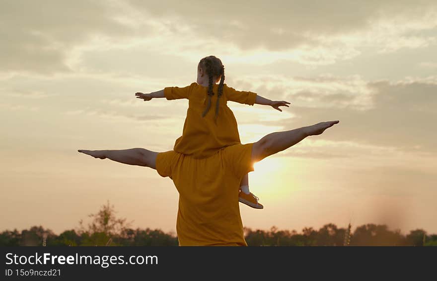 child sits on her father shoulders dreaming of flying at sunset, girl glare of the sun wants to be pilot, play with dad