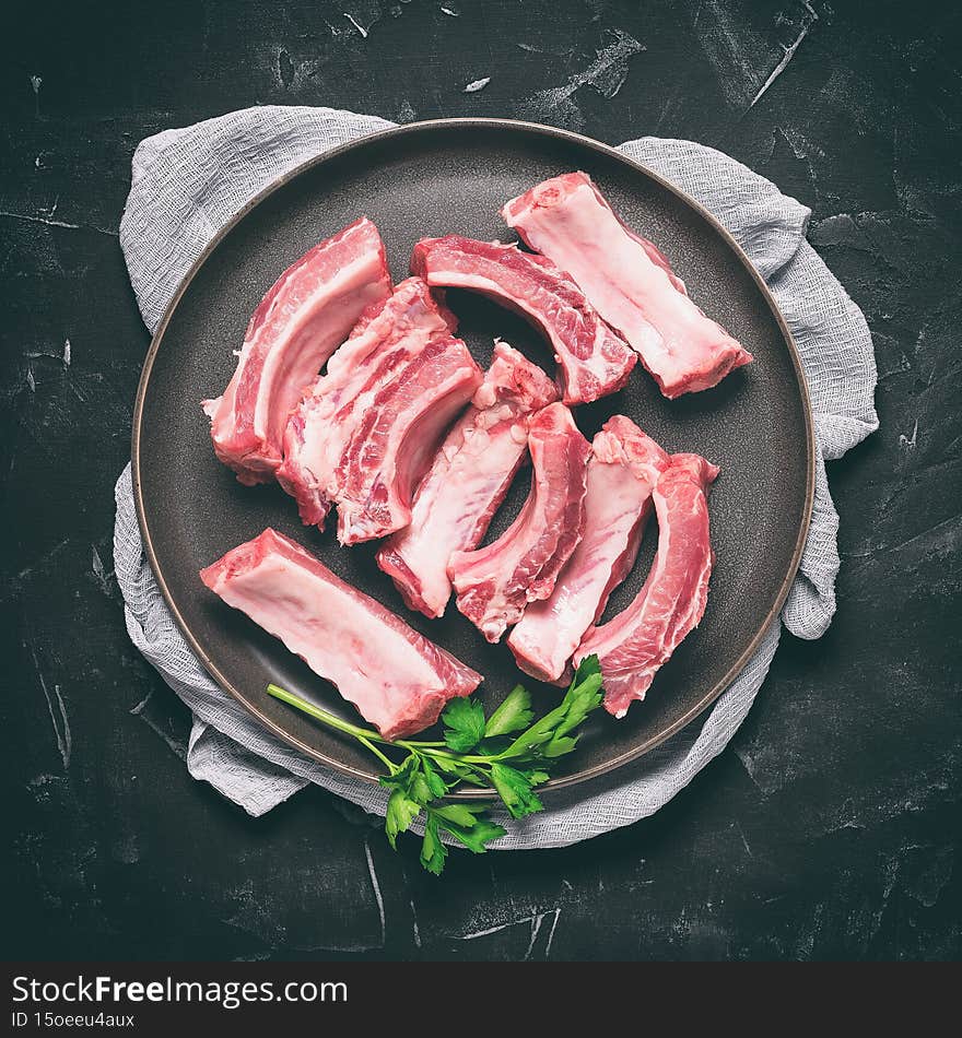 Raw pork ribs slices on a plate, black stone background. Top view, flat lay. Square toned photo.