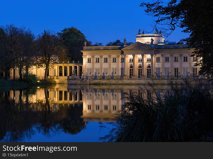 The Palace on the Isle in Lazienki Park, city of Warsaw, Poland. Royal summer residence from 18th century, Neoclassical northern facade illuminated at night with reflection in lake. The Palace on the Isle in Lazienki Park, city of Warsaw, Poland. Royal summer residence from 18th century, Neoclassical northern facade illuminated at night with reflection in lake