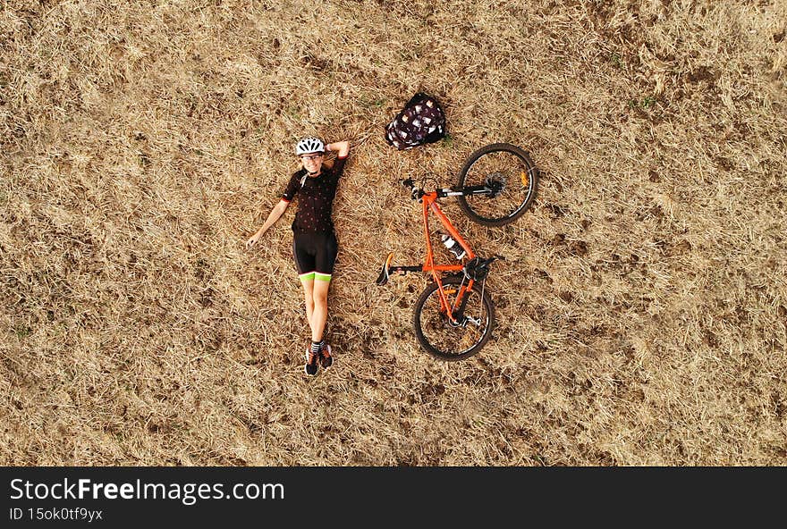Aerial vacation trip photo of cyclist girl lying on autumn field with orange bicycle. Drone top view.