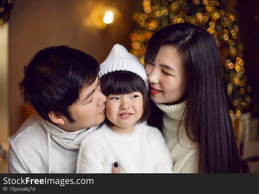 korean family mom dad and daughter child sitting at the Christmas tree with garlands in studio at home