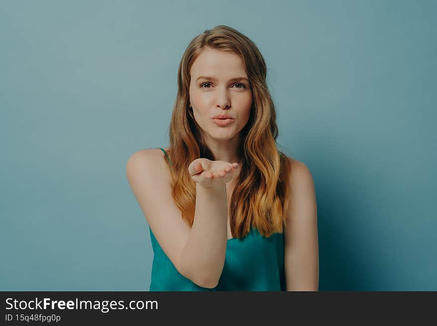 Pretty candid girl blowing air kiss and expressing love while standing isolated on blue background