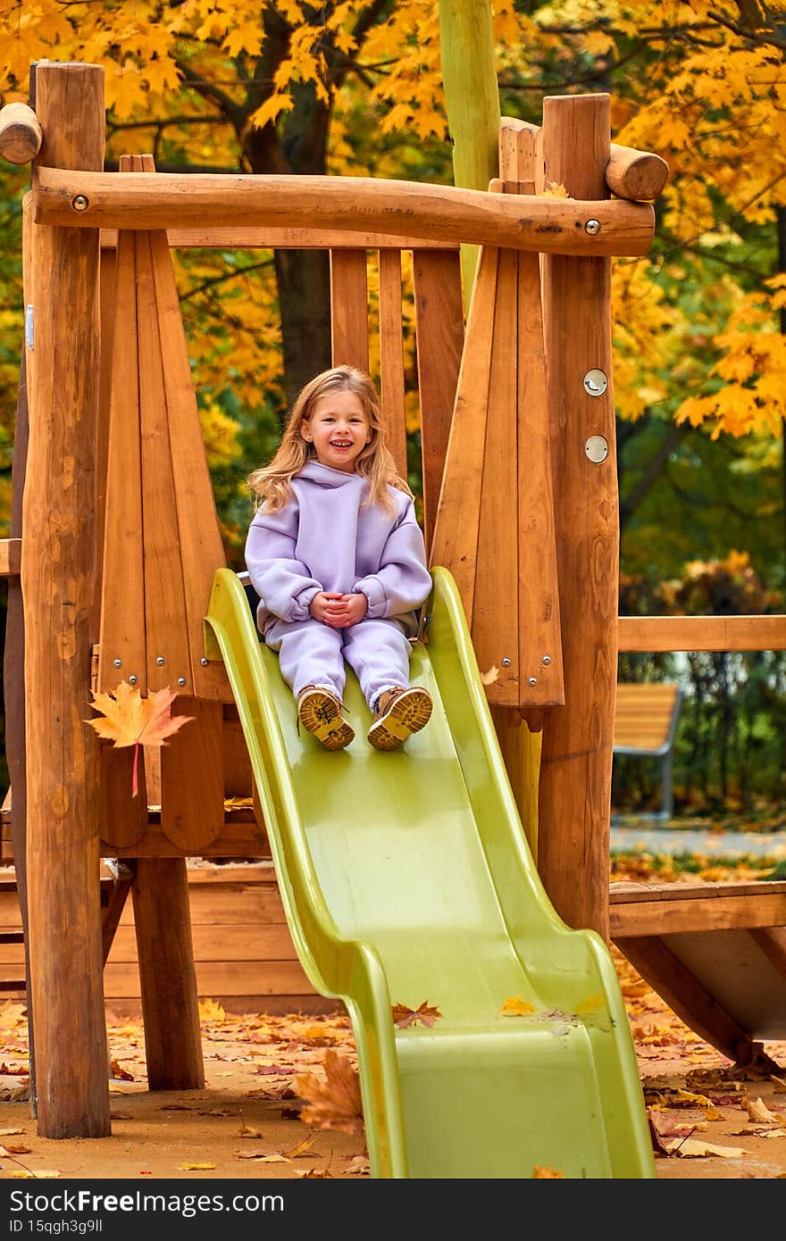 The girl went down the hill. The child plays on the playground in the fall. Wooden platform on the territory of the new house. Happy childhood. Yellow foliage on the trees on a sunny day.