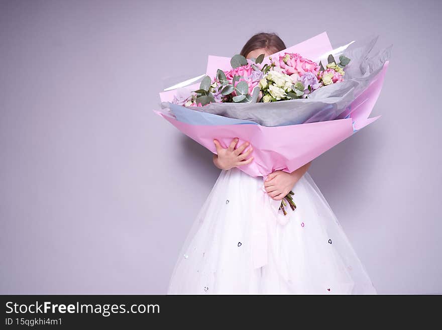 A girl in a white dress stands to the side and holds a bouquet of flowers, covering her face. Holiday concept. High quality photo