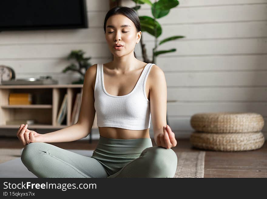 Mindfulness and meditation concept. Young asian woman doing workout at home, yoga meditation in living room on floor mat