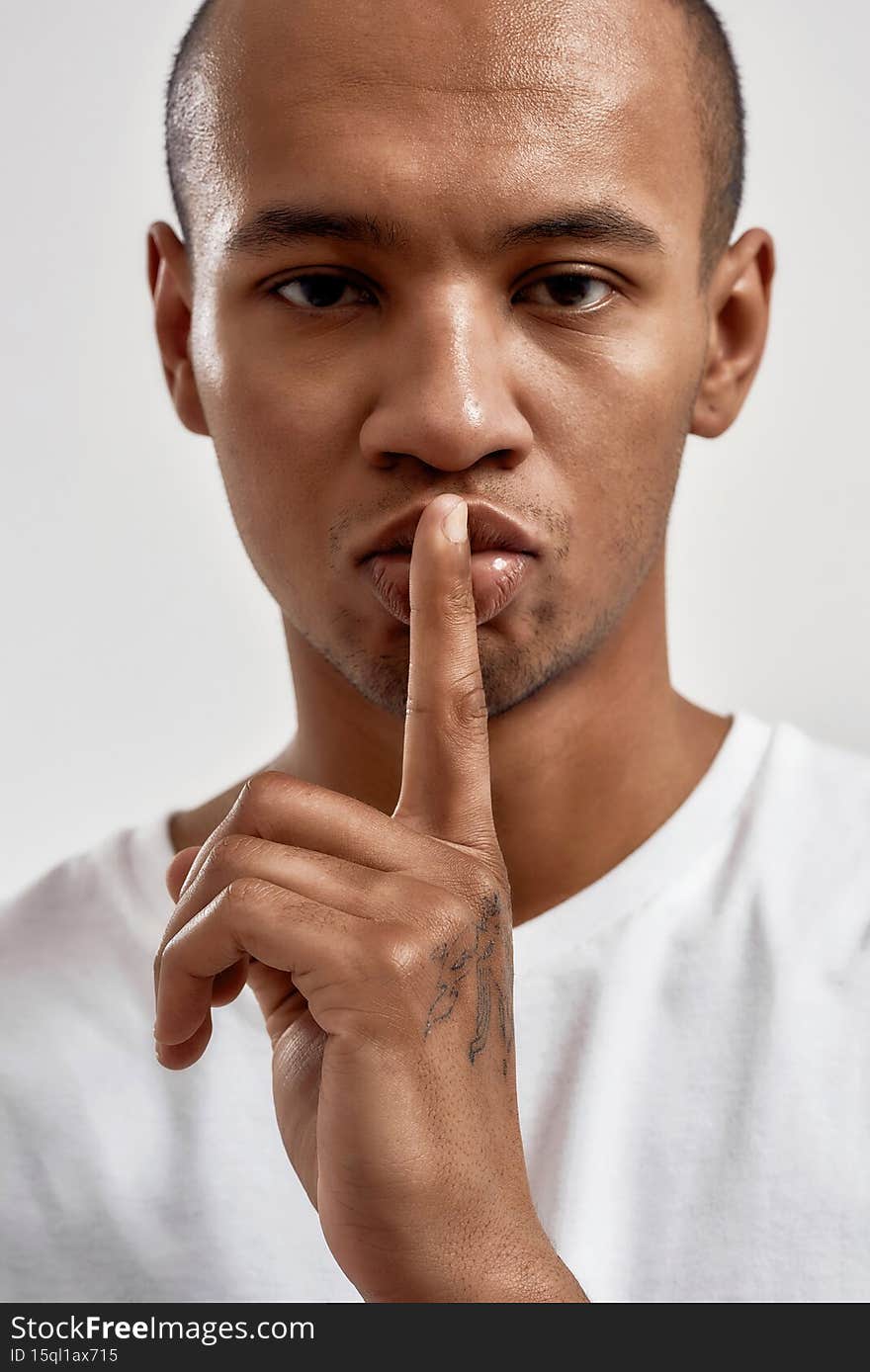 Portrait of dark skinned young guy showing shh gesture, keeping a secret, posing isolated over white background