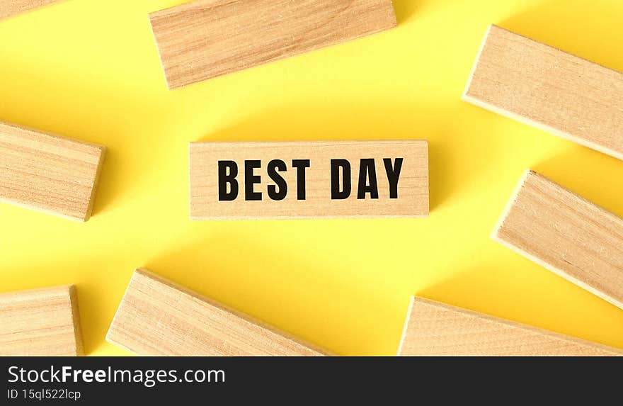 The word BEST DAY is written on a wooden blocks on a yellow background.