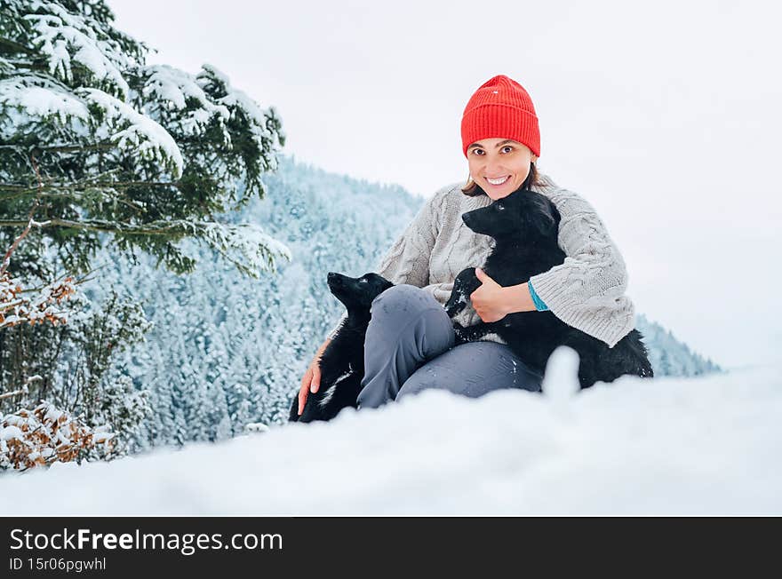 A young woman in warm clothes walking her 2 dogs in snowy mountain outdoor. Female laughing, hugging, and playing with pets. Human and pets winter season concept image
