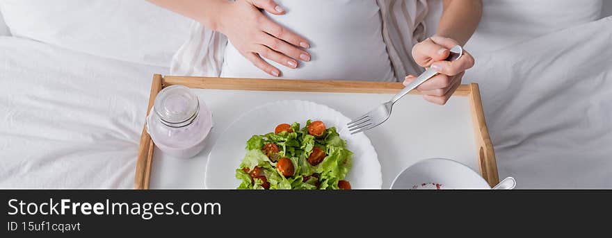 cropped view of pregnant woman holding fork near meal on tray, banner,stock image