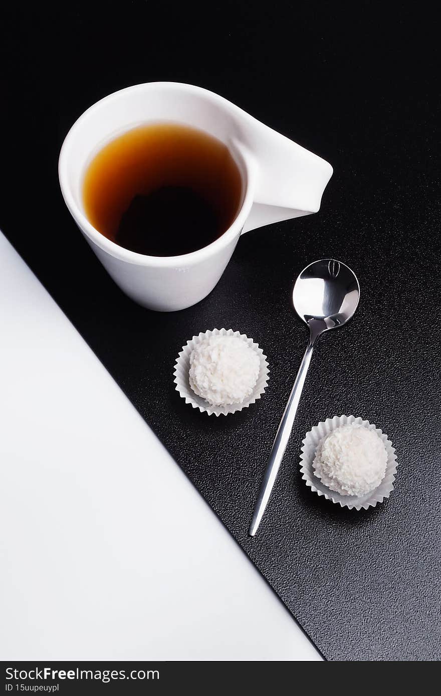 Creative concept of white tea cup with spoon and candy on black and white background. Geomtric food and drink concept