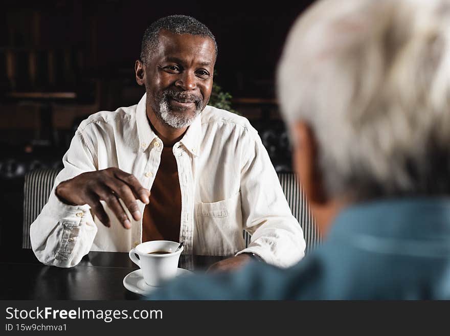 smiling senior african american man looking at blurred friend near cup of coffee,stock image