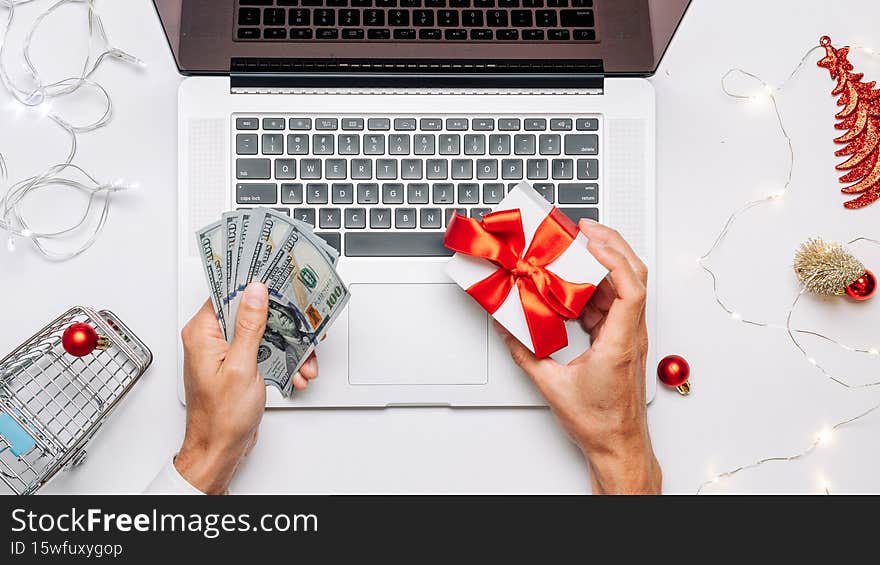 Online christmas. Gift box red ribbon, trolley and laptop, money in flat lay internet shopping composition. Winter Xmas