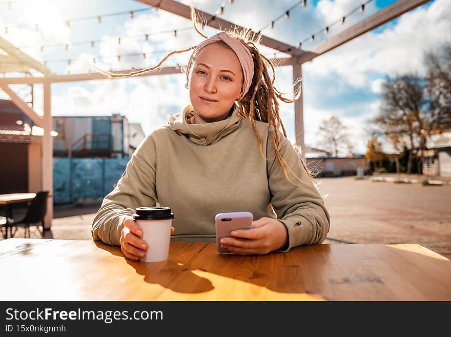 Portrait of a young woman with dreadlocks drinking coffee in a cafe and using a smartphone. The concept of business and