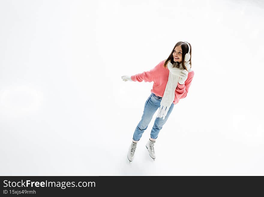 high angle view of positive young woman in ear muffs and scarf skating on ice rink,stock image