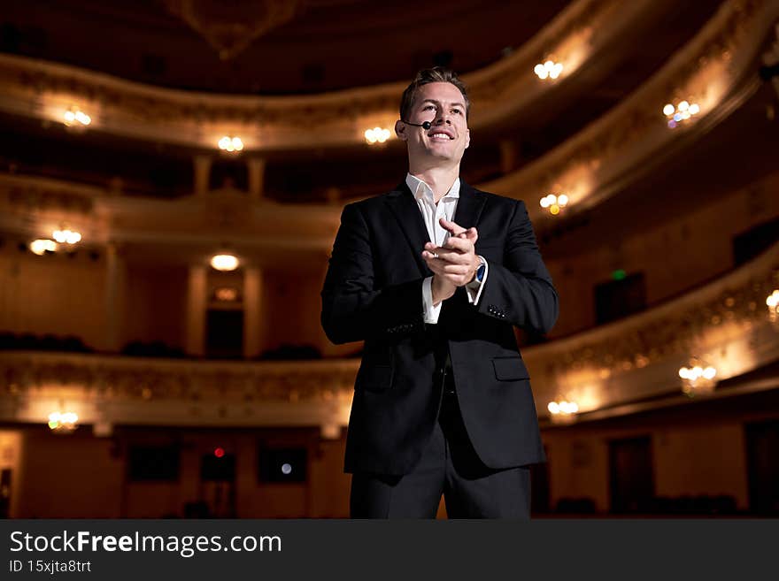 Talented business couch standing on stage clapping hands, keep hands together after good successful performance, looking at audience, wearing classic formal suit, handsome and elegant. Talented business couch standing on stage clapping hands, keep hands together after good successful performance, looking at audience, wearing classic formal suit, handsome and elegant