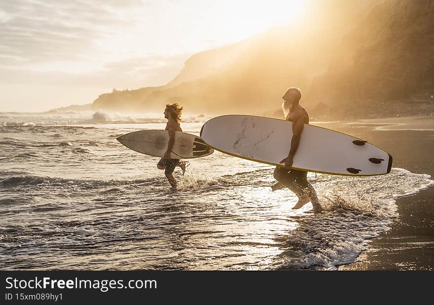 Happy fit friends surfing together on tropical beach at sunset time