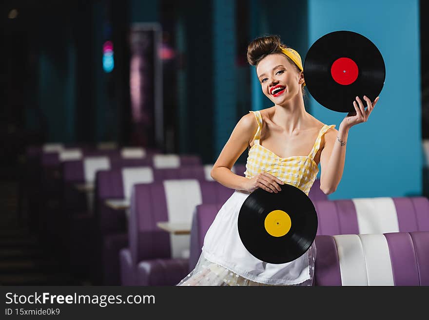pin up woman with red lips holding retro vinyl records and smiling in cafe,stock image